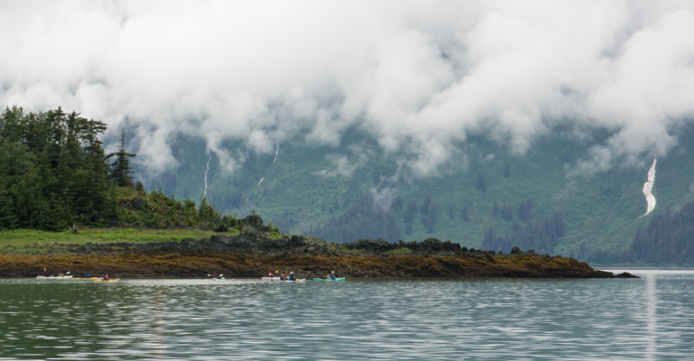 A picture of the coastline of Ketchikan with clouds, mist and the Tongass National Forest in the background.